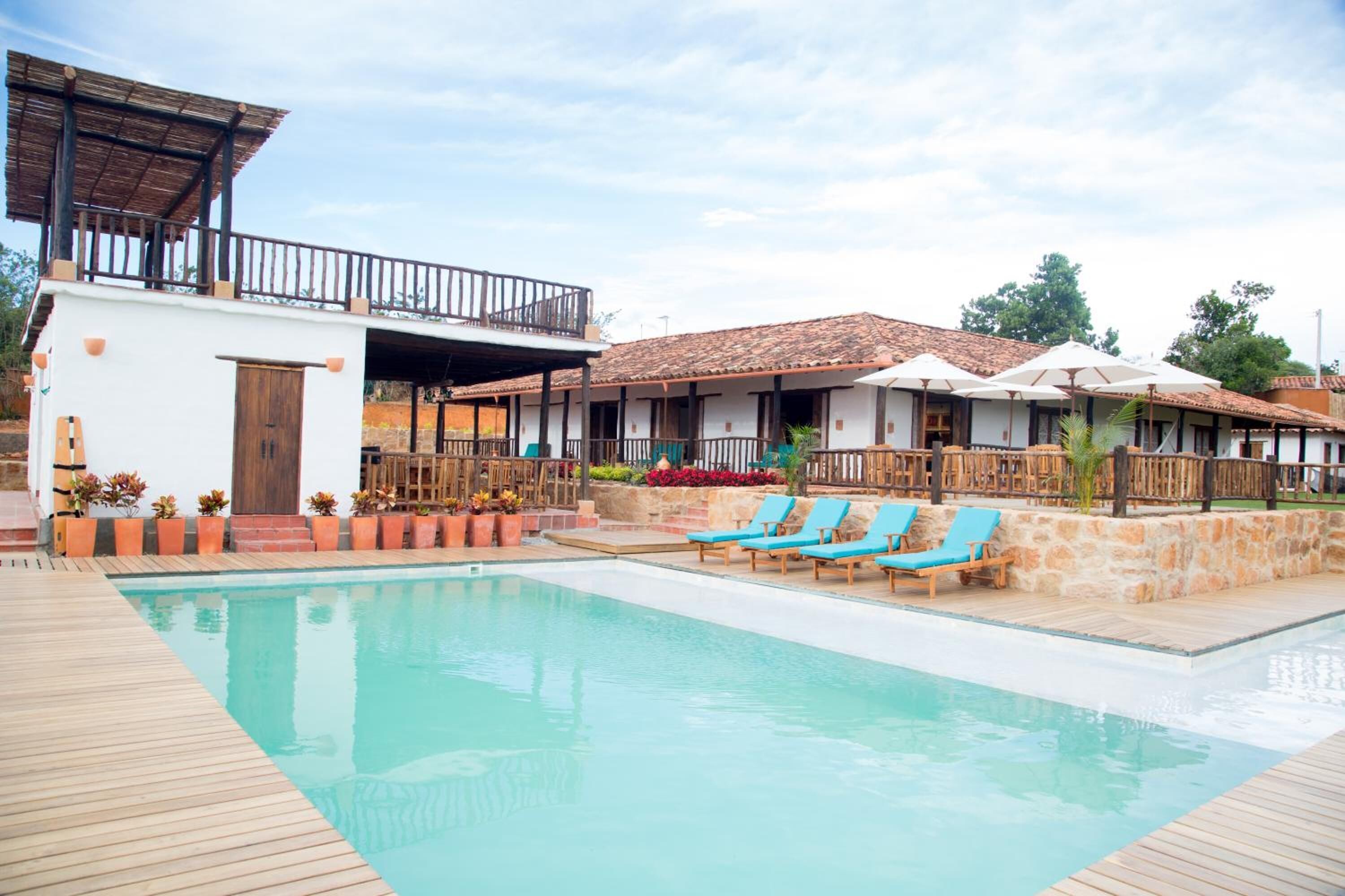 Un área de piscina con sillones reclinables, una terraza de madera y un edificio con balcón.