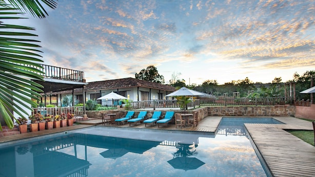 A swimming pool with lounge chairs and umbrellas, surrounded by a wooden deck and a building with a balcony. - Hotel Boutique Venturi (Barichara)