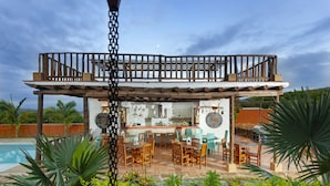 A covered outdoor dining area with wooden furniture and a pool in the background. - Hotel Boutique Venturi (Barichara)