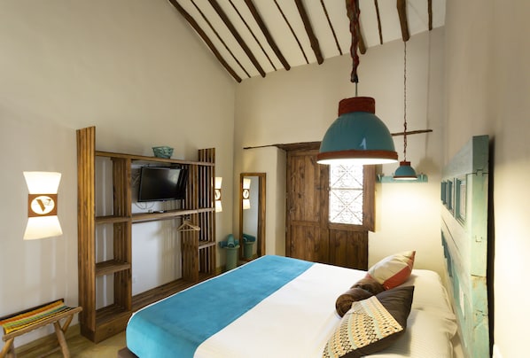 A bedroom with a bed, a TV, wooden furniture, and a hanging light fixture.