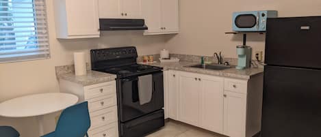A kitchen with white cabinets, a black stove, a black refrigerator, a blue microwave, a sink, and a small table with blue chairs.