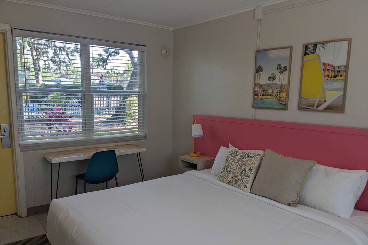 A hotel room with a bed, a desk, a chair, and a window with blinds.