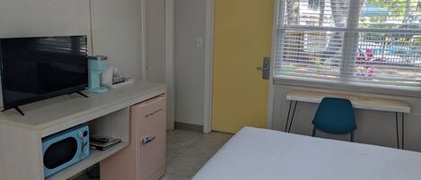 A room with a bed, a desk, a television, a microwave, and a refrigerator.