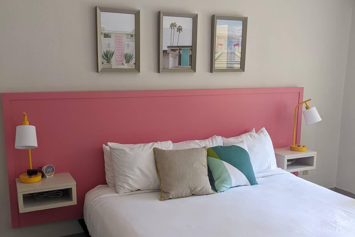 A neatly arranged hotel room with a large bed, a pink headboard, and three framed pictures on the wall.