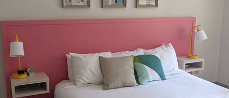 A neatly arranged hotel room with a large bed, a pink headboard, and three framed pictures on the wall.