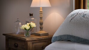 A wooden bedside table with a lamp, a glass jar, and a vase with white flowers. - French Cottage (Hepburn Springs)