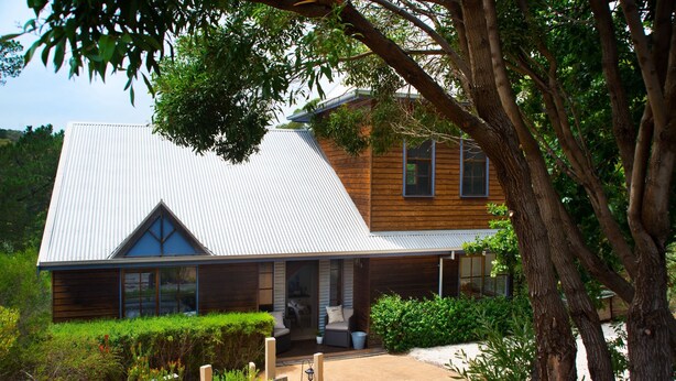 A two-story house with a sloped metal roof, wooden siding, and a front porch with seating. - French Cottage (Hepburn Springs)