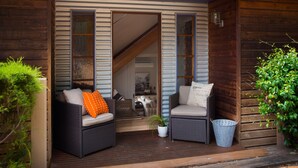 A wooden porch with two wicker chairs, a potted plant, and a blue basket. - French Cottage (Hepburn Springs)