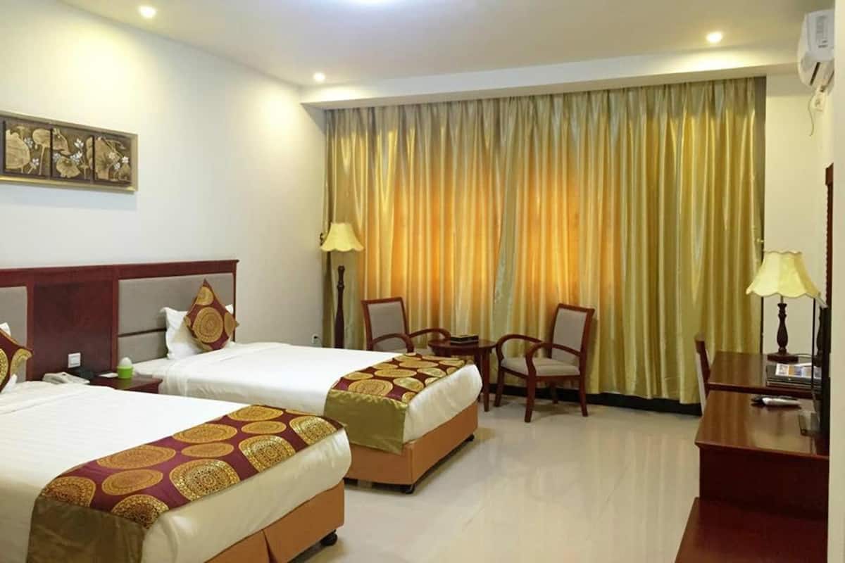A hotel room with two beds, a desk, chairs, and a large window with curtains.