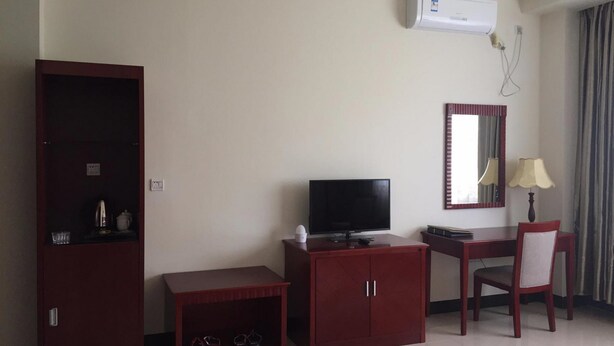 A hotel room with a TV, a desk, a chair, a wardrobe, a small table with glasses, and an air conditioning unit. - Meida Hotel & Restaurant (Nuku'alofa)