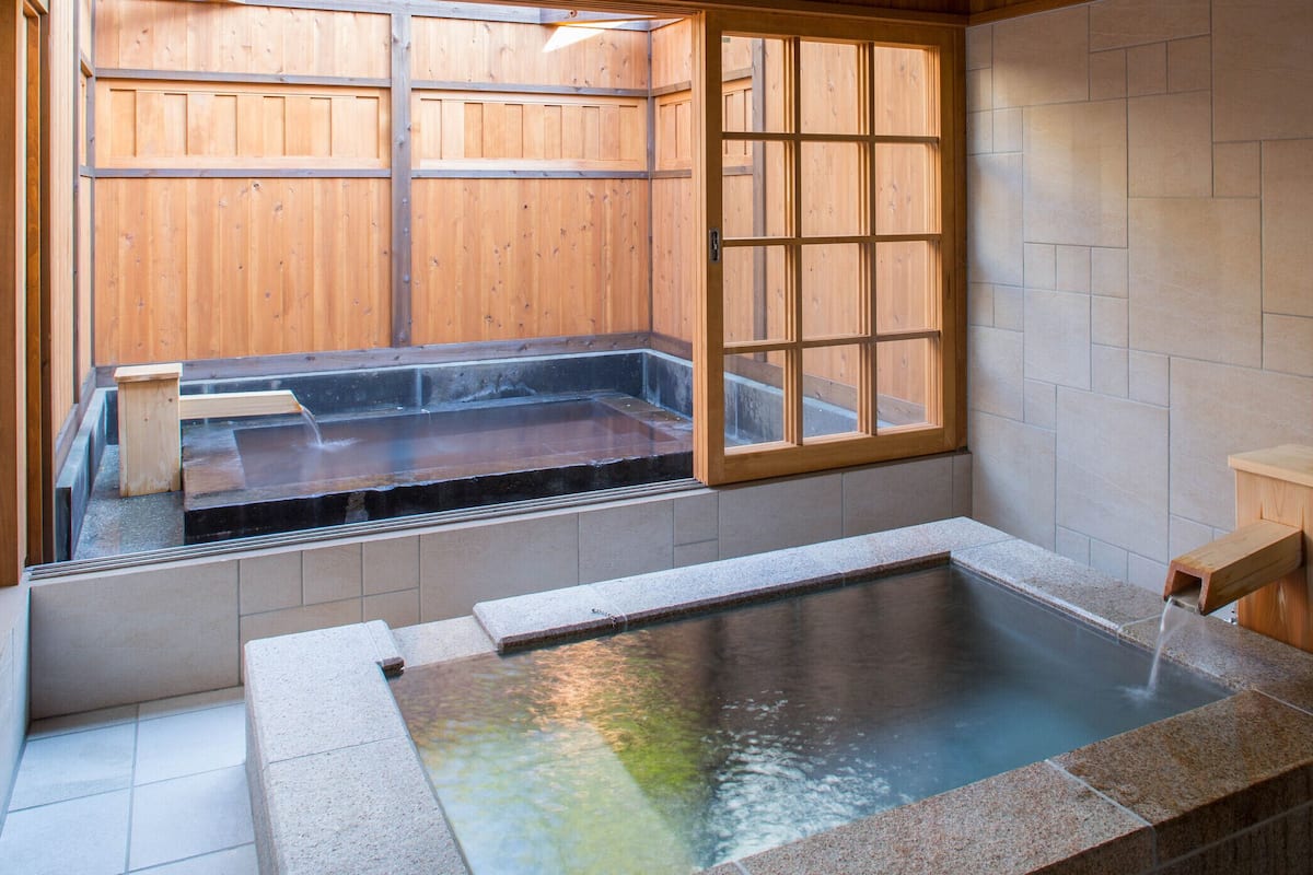A hot spring bath with a wooden window and tiled walls.
