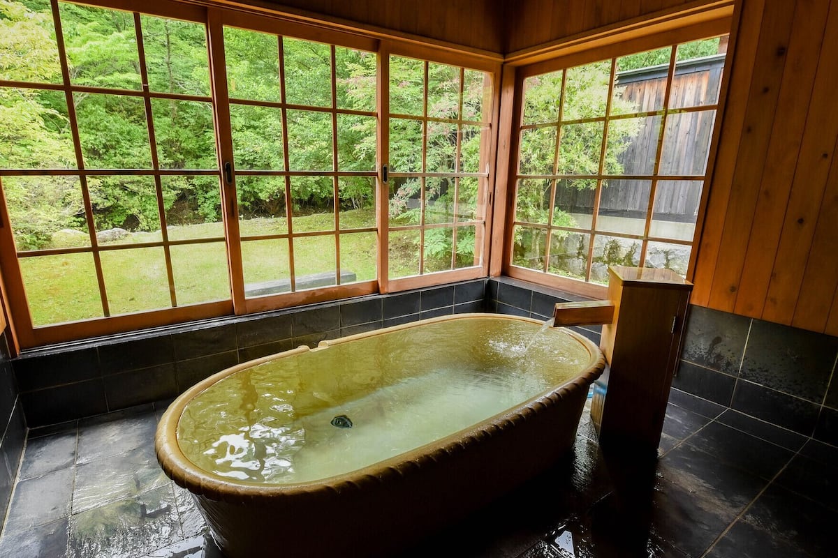 Une chambre avec une baignoire, de grandes fenêtres et une vue sur la verdure.
