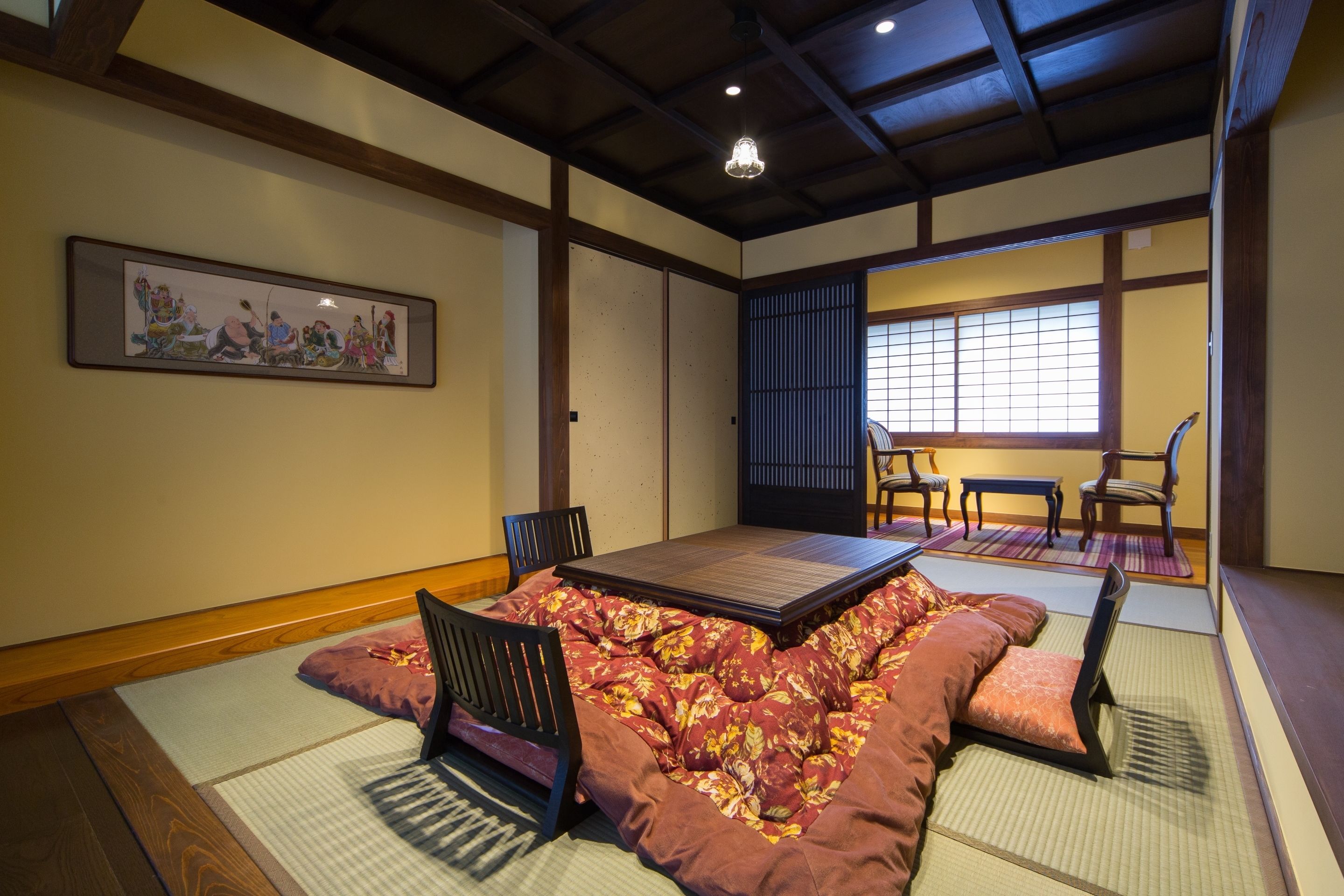 A tatami mat room with a low table and chairs, a shoji screen, and a traditional Japanese painting on the wall.