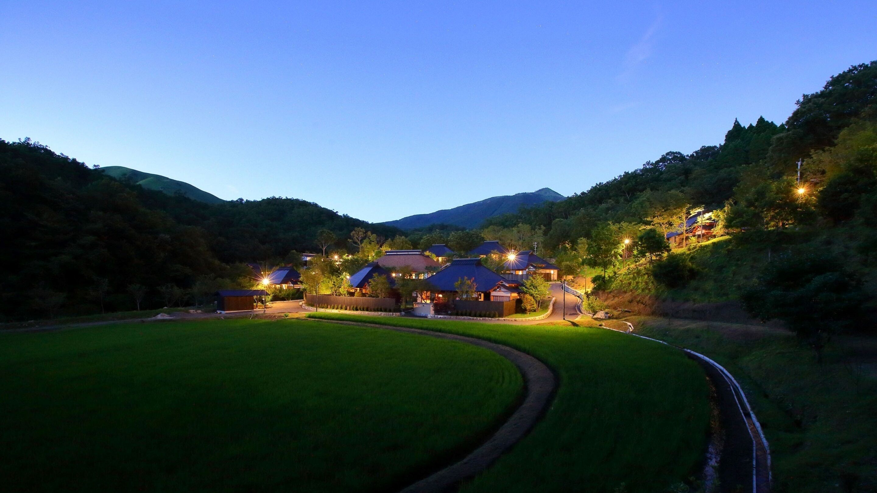 A traditional Japanese-style hotel with multiple buildings, a well-maintained lawn, and a winding road.