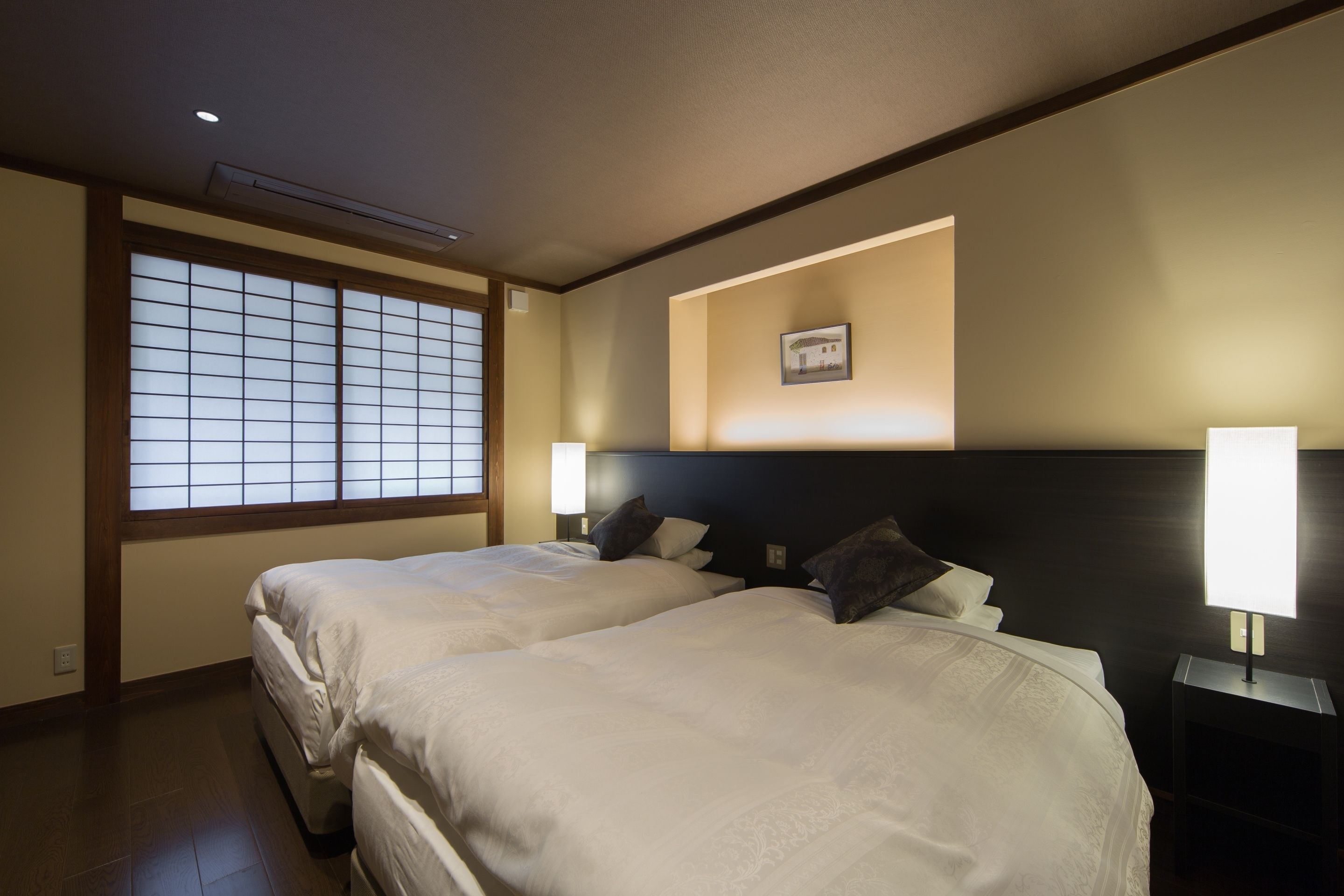 Ett hotellrum med två sängar, ett stort fönster med utsikt och en tavla som hänger på väggen.