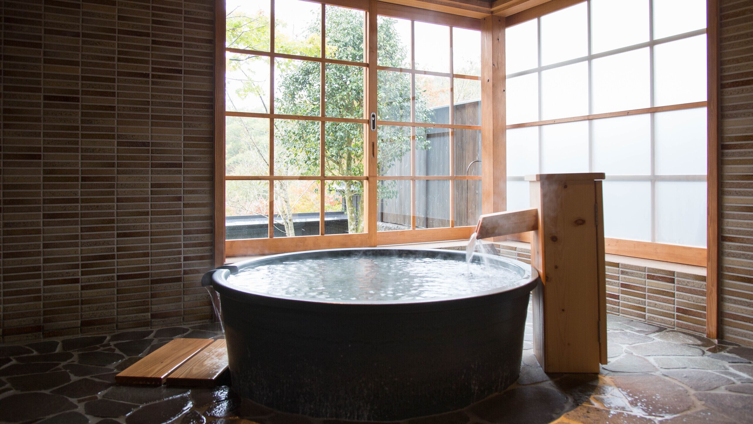 Ein Whirlpool in einem Raum mit großem Fenster, Steinboden und Holzwänden.