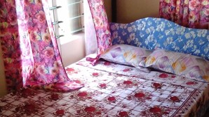 Un lit avec une literie et des rideaux à motifs floraux, une fenêtre avec des stores et un sol carrelé.