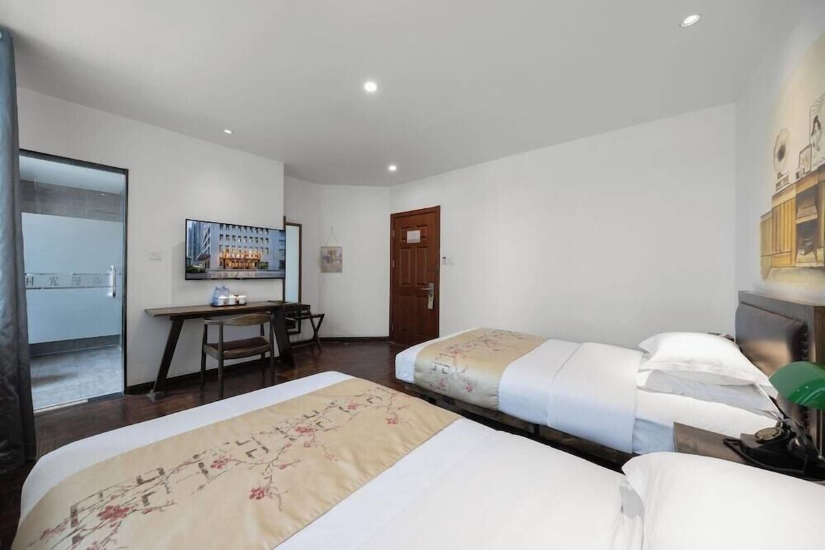 A hotel room with two beds, a desk with a chair, a television, and a door.
