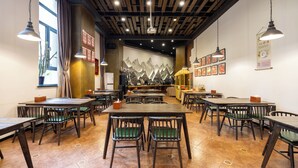 A restaurant with wooden tables and chairs, a mural of mountains on the wall, and hanging lights.