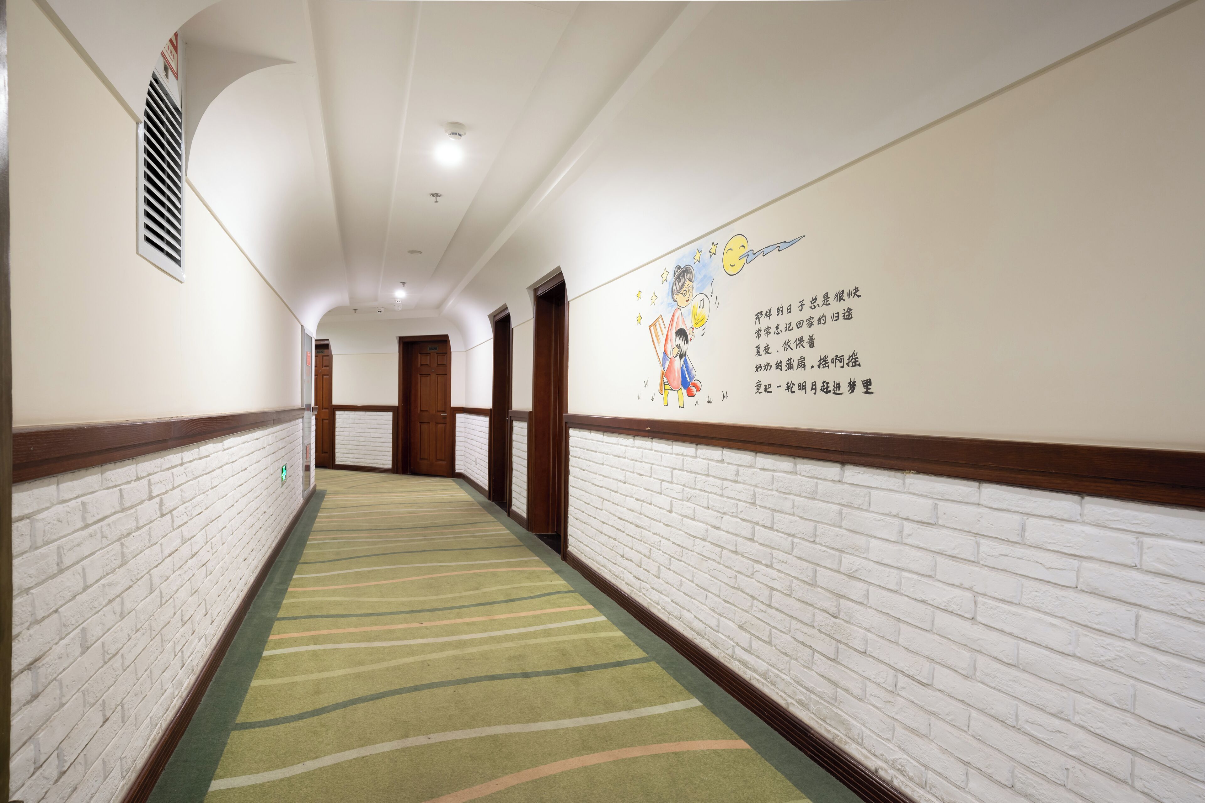 Un couloir d’hôtel avec un mur en briques, une moquette à motifs et une porte au fond.