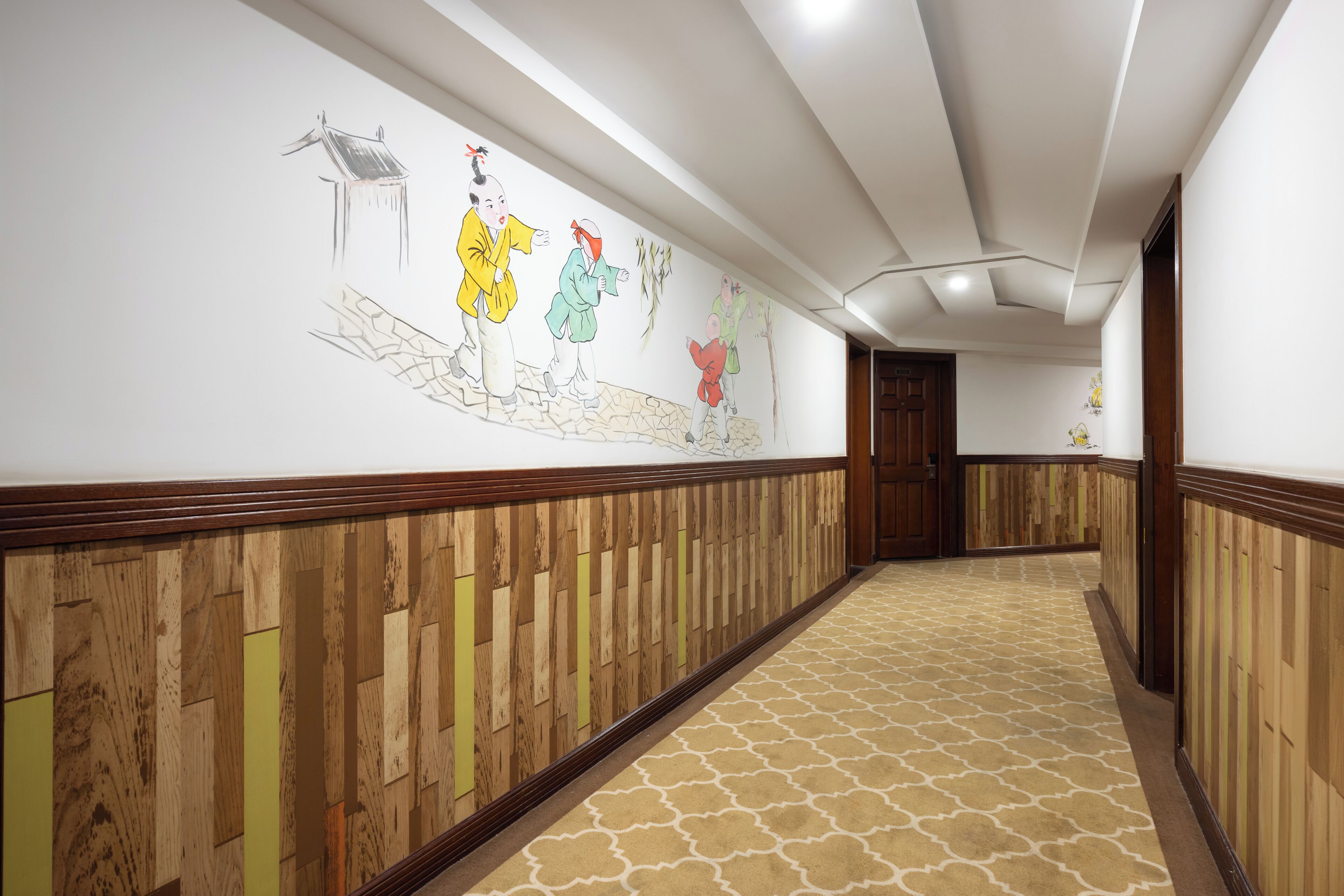A hallway with wooden paneling and a patterned carpet, leading to a door at the end.