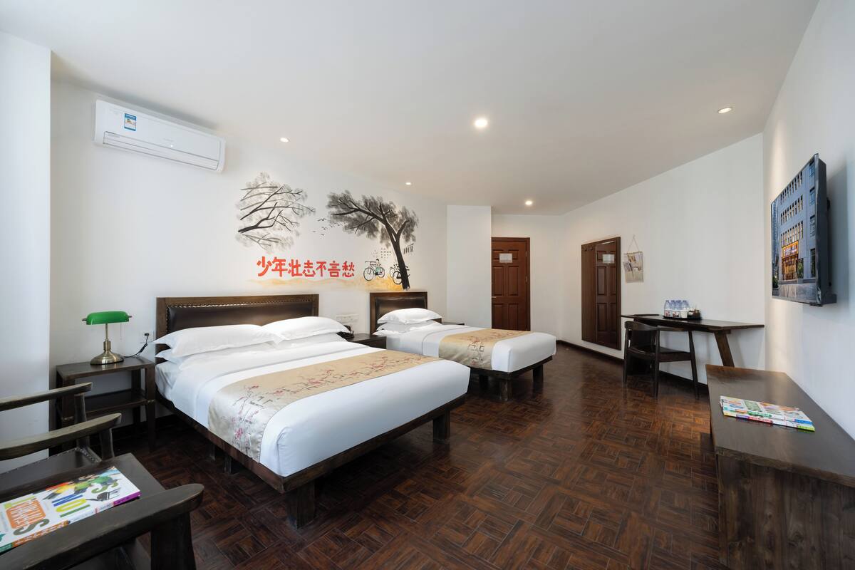 A hotel room with two beds, a desk, a chair, a table, and a wall-mounted TV.