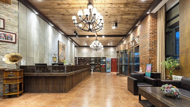 A spacious lobby with a wooden ceiling, a large chandelier, a reception desk, and a seating area with a sofa and a table.