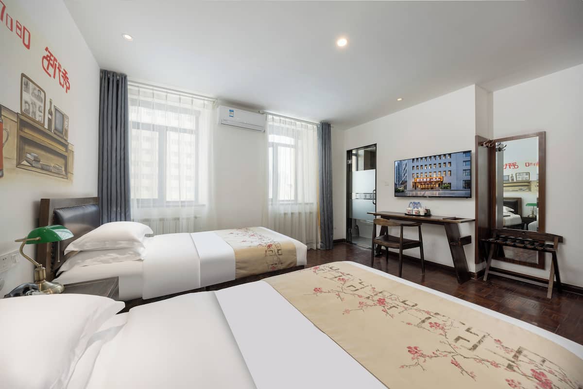 A hotel room with two beds, a desk, a chair, a TV, and a mirror.