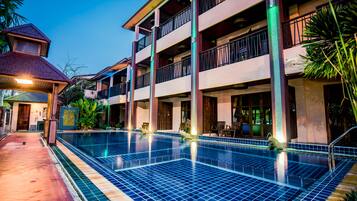 A hotel with a swimming pool, multiple balconies, and a covered walkway.