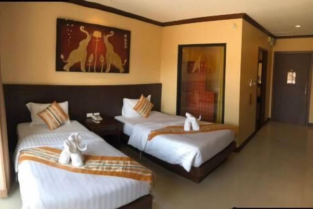 A hotel room with two beds, a painting on the wall, and a door leading to another room.