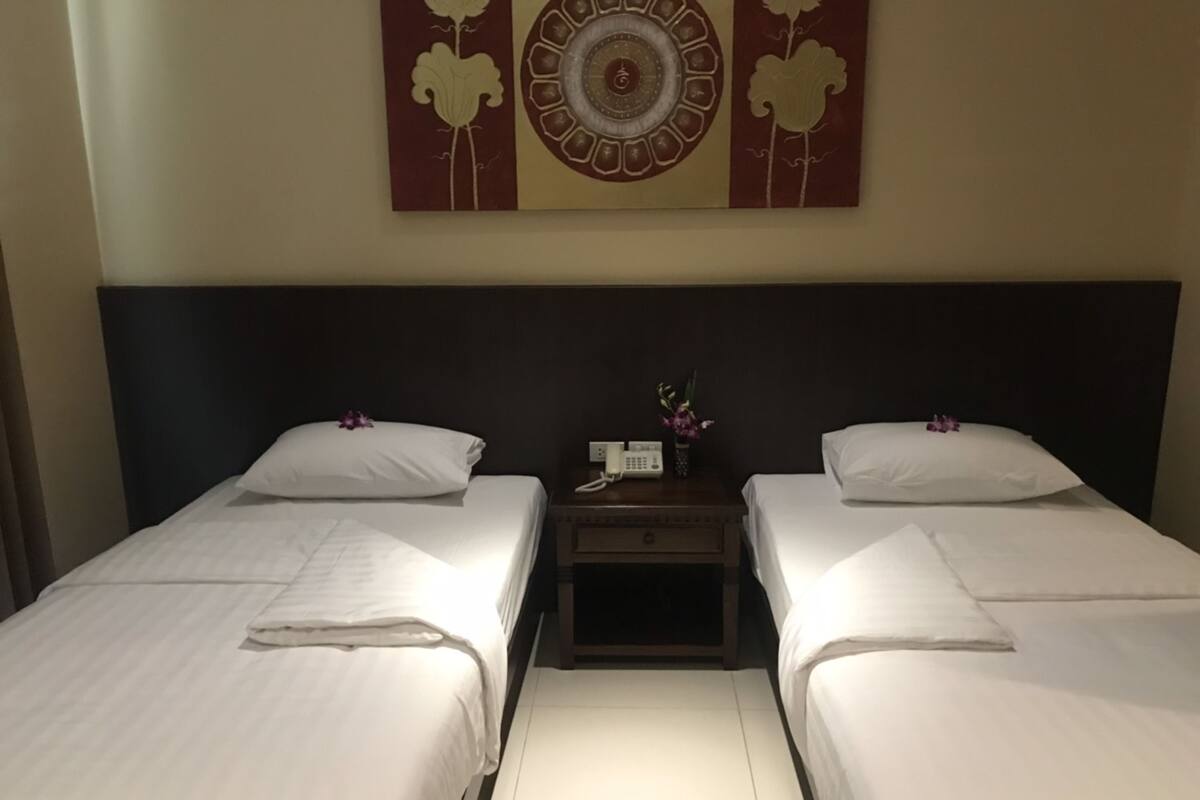 A hotel room with two single beds, a nightstand with a phone and a vase of flowers, and a wall decoration above the beds.