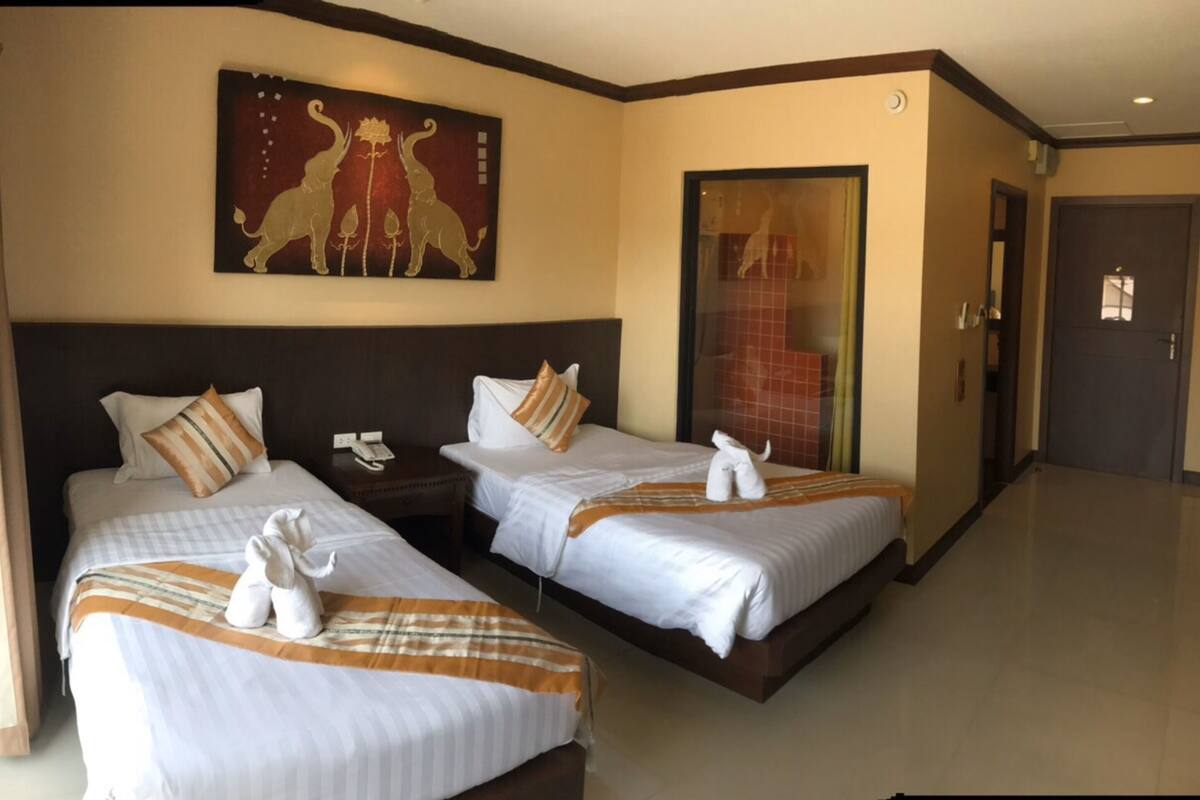 A hotel room with two beds, a painting on the wall, a telephone on a nightstand, and a door leading to another room.