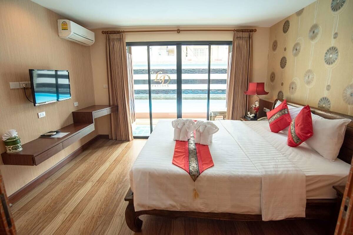 A hotel room with a bed, a TV, a desk, and a view of the beach through the sliding doors.
