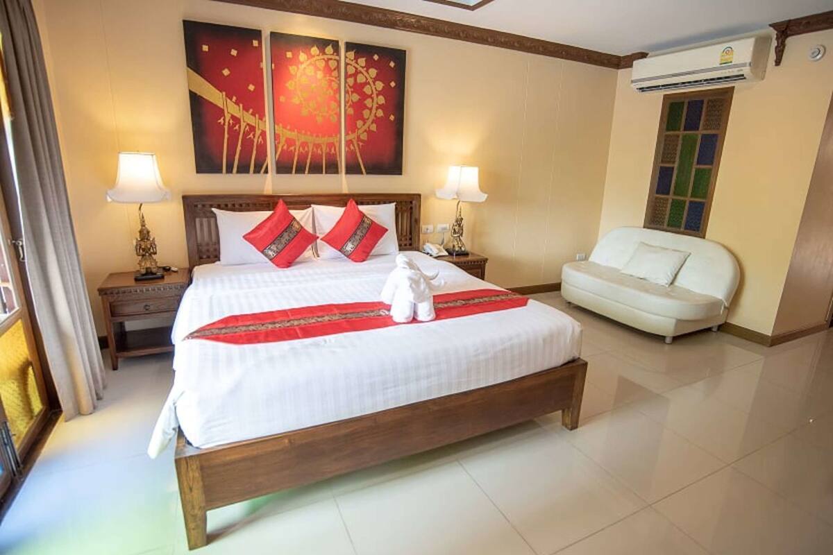 A hotel room with a large bed, two bedside lamps, a white sofa, and a wall-mounted air conditioner.