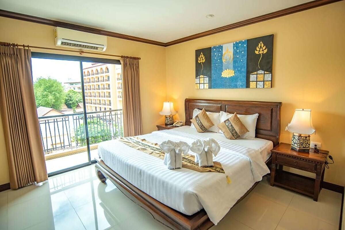 A hotel room with a large bed, two bedside tables with lamps, a balcony with curtains, and a painting on the wall.
