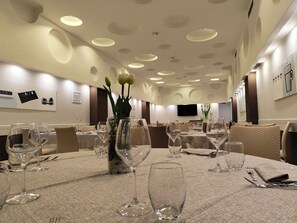 Un comedor de hotel con mesas redondas, sillas y un televisor montado en la pared.