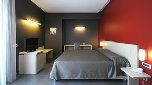 A modern hotel room with a bed, desk, and television. - Hotel Bruman - Casoria (Casoria)