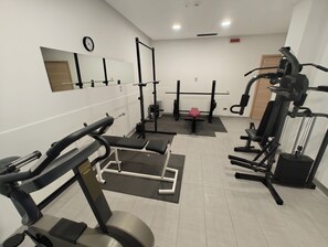 Un gimnasio con diversos equipos de ejercicio, como una prensa de banca, una estructura para sentadillas y un banco para pesas.