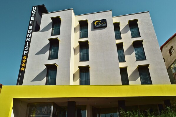 Un moderno edificio de hotel con un letrero que dice "Sunrise Hotel" y un logotipo que muestra una luna creciente y estrellas.