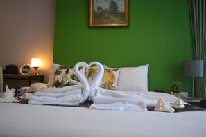 A neatly made bed with towels arranged in a swan shape, a painting on the wall, and a green wall.
