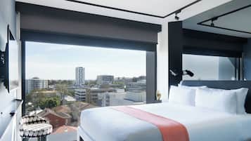 Habitación de hotel moderna con una cama grande, vistas a la ciudad y un balcón con una silla.