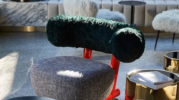 A modern living room with a grey, textured ottoman, a green, furry chair, and a red stool.