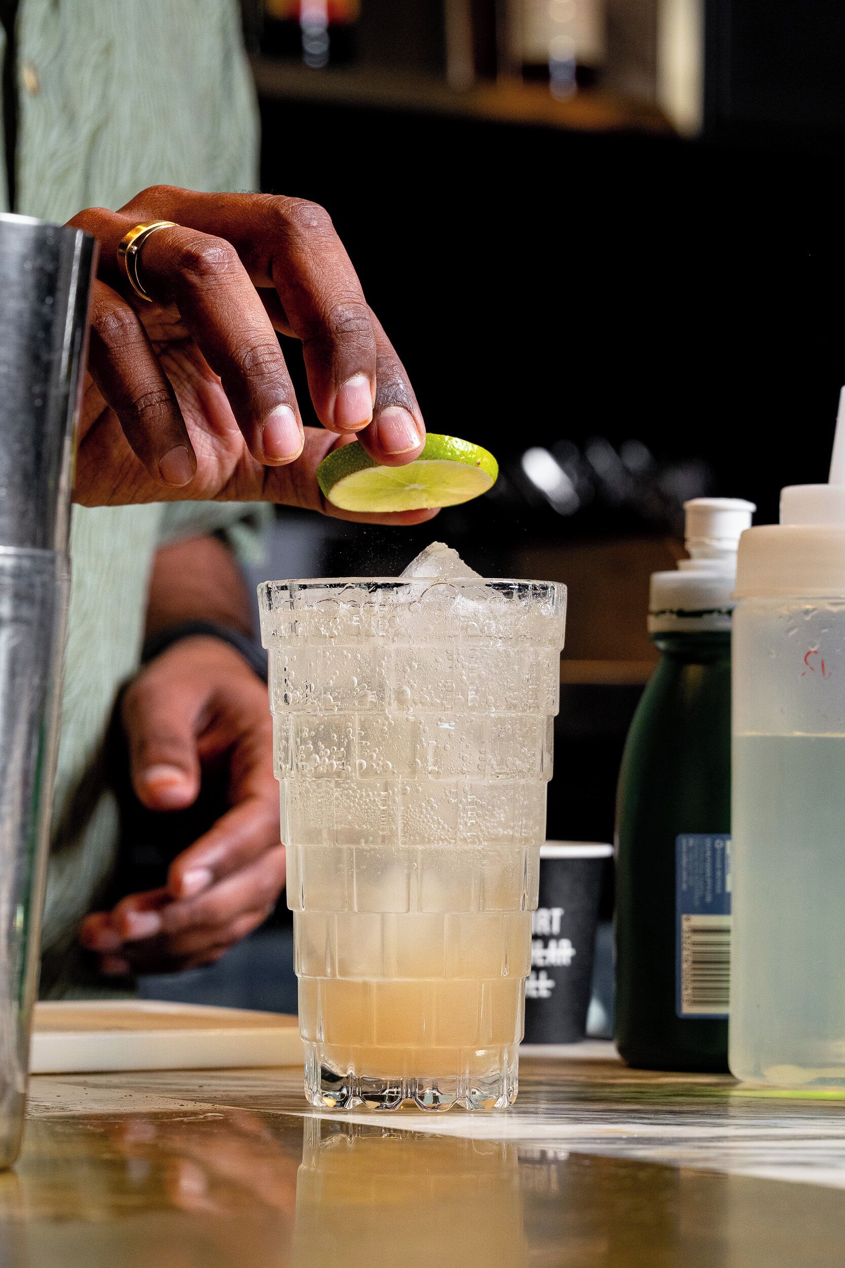 A hand squeezing a lime into a glass with ice cubes.