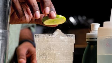 A hand squeezing a lime into a glass with ice cubes.