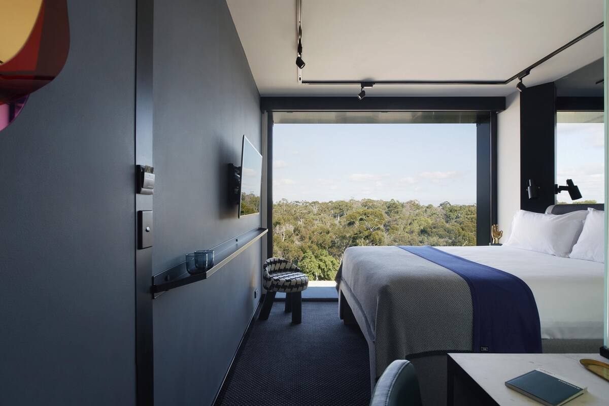 Une chambre d’hôtel moderne avec un grand lit, un bureau et une vue sur la forêt.