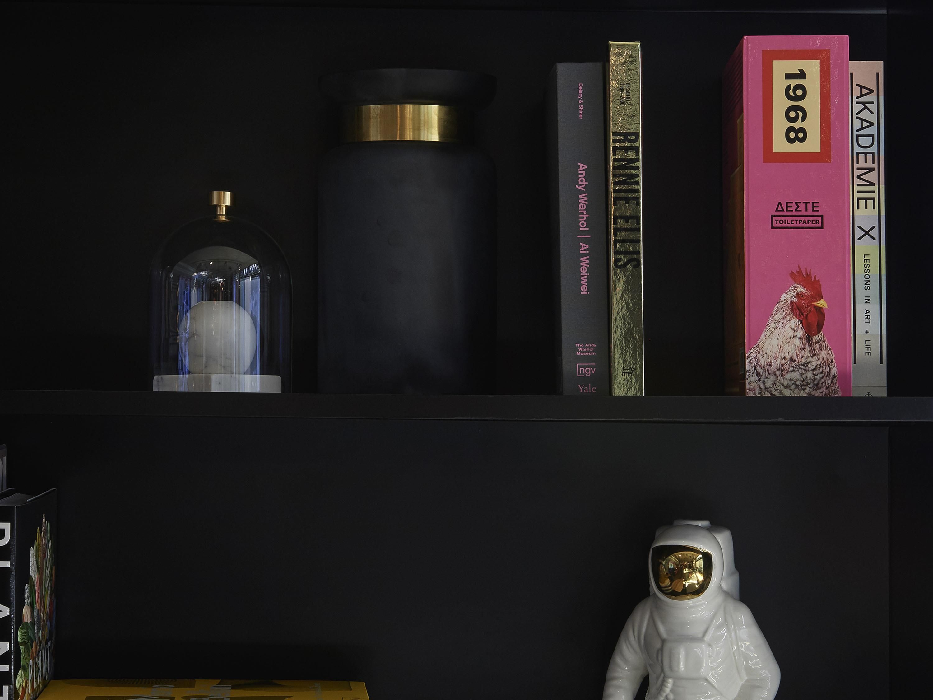 A bookshelf with books, a glass dome object, and a white astronaut figurine.