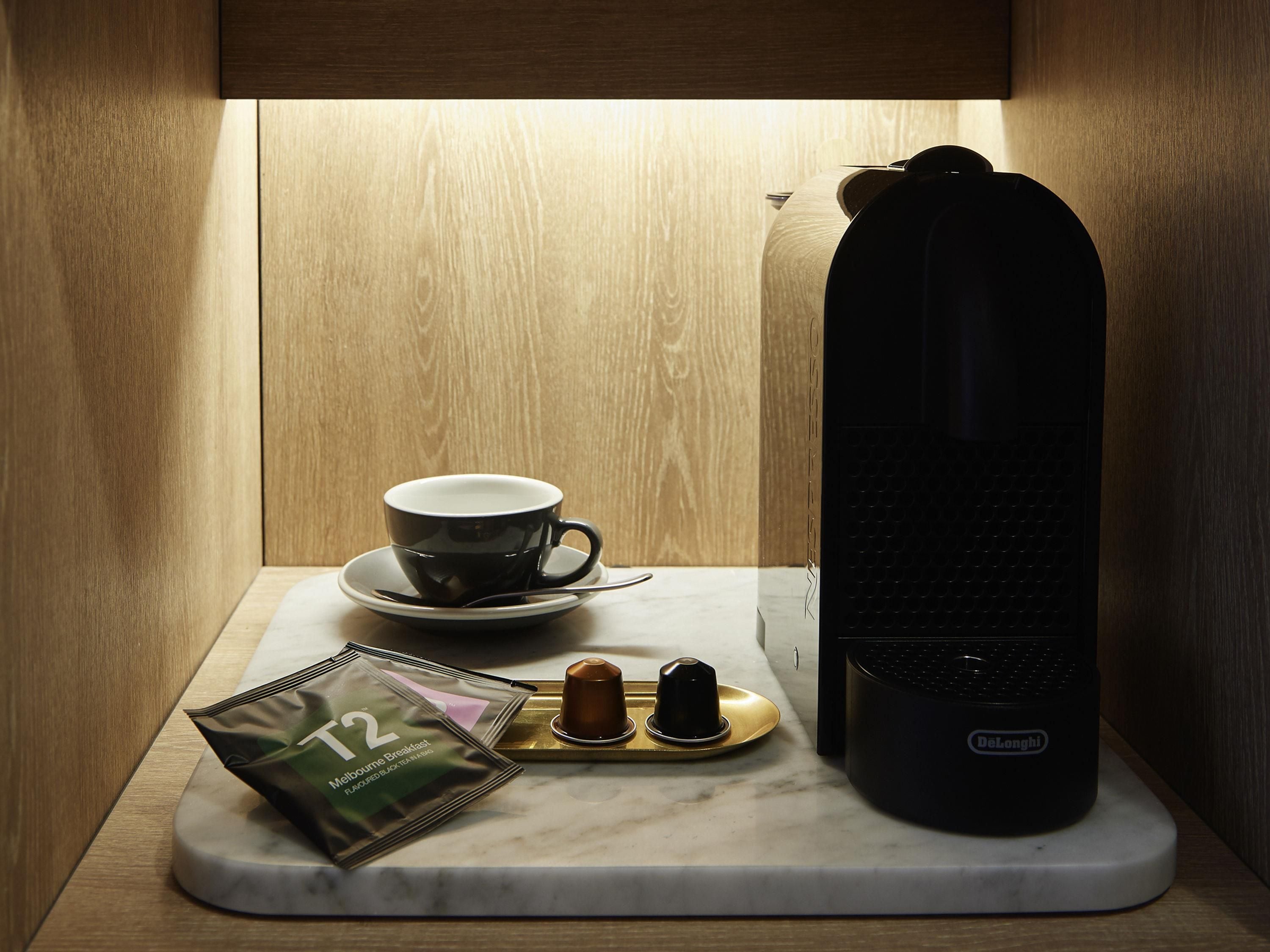 A coffee maker, a cup, and a packet of coffee on a marble countertop.