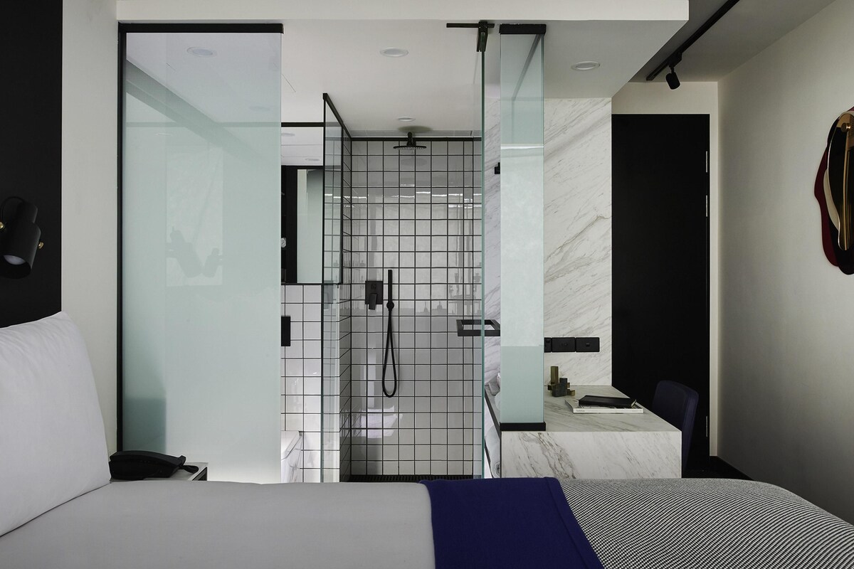 A modern hotel room with a bed, a shower area, and a small desk.