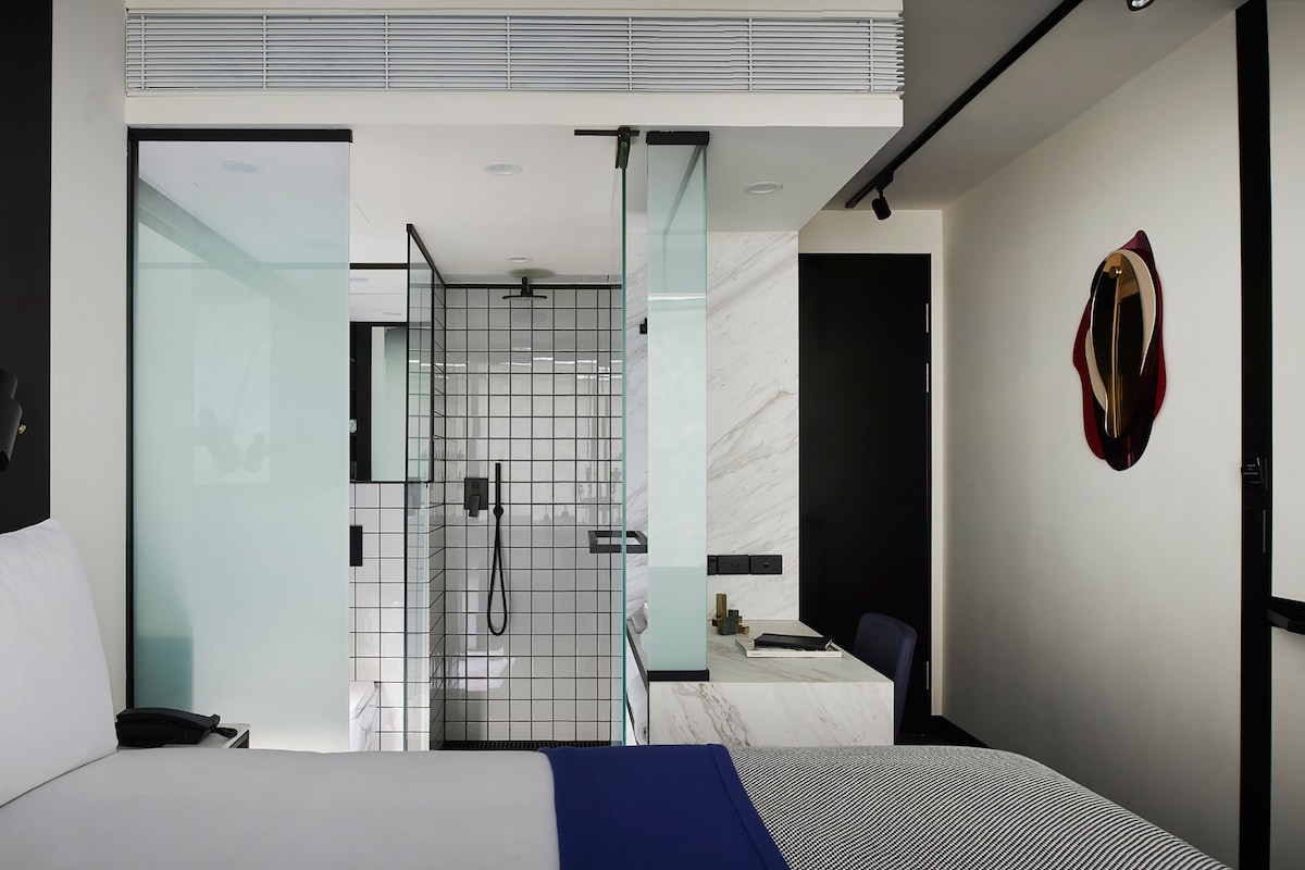 A modern hotel room with a bed, a desk, and a shower area.