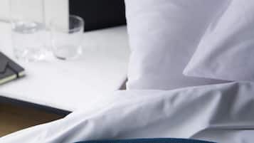 A bed with white sheets and a blue blanket, a bedside table with a glass of water, and a black object on the table.